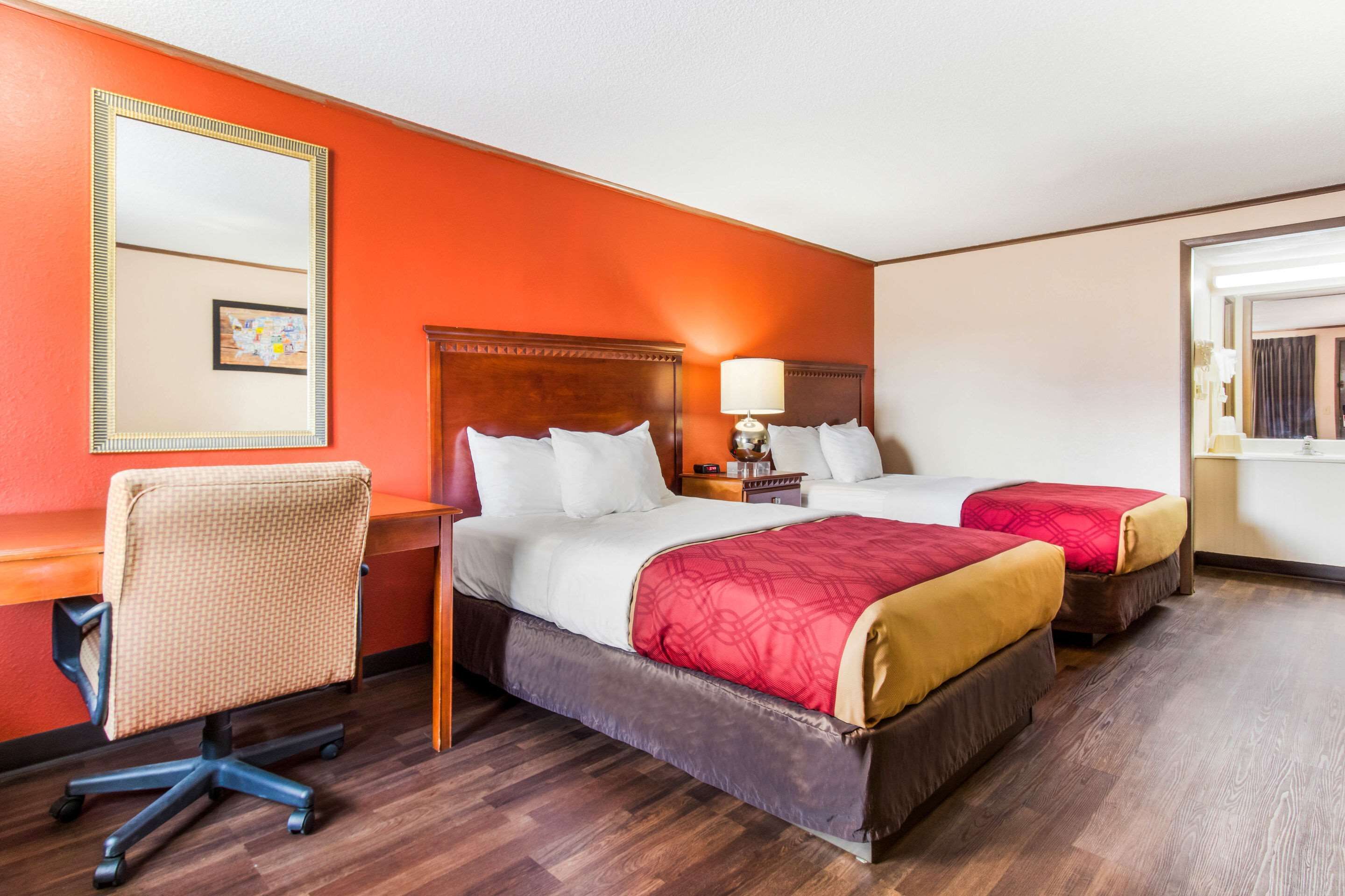 Habitación de hotel con dos camas, un escritorio, una silla y un espejo grande.