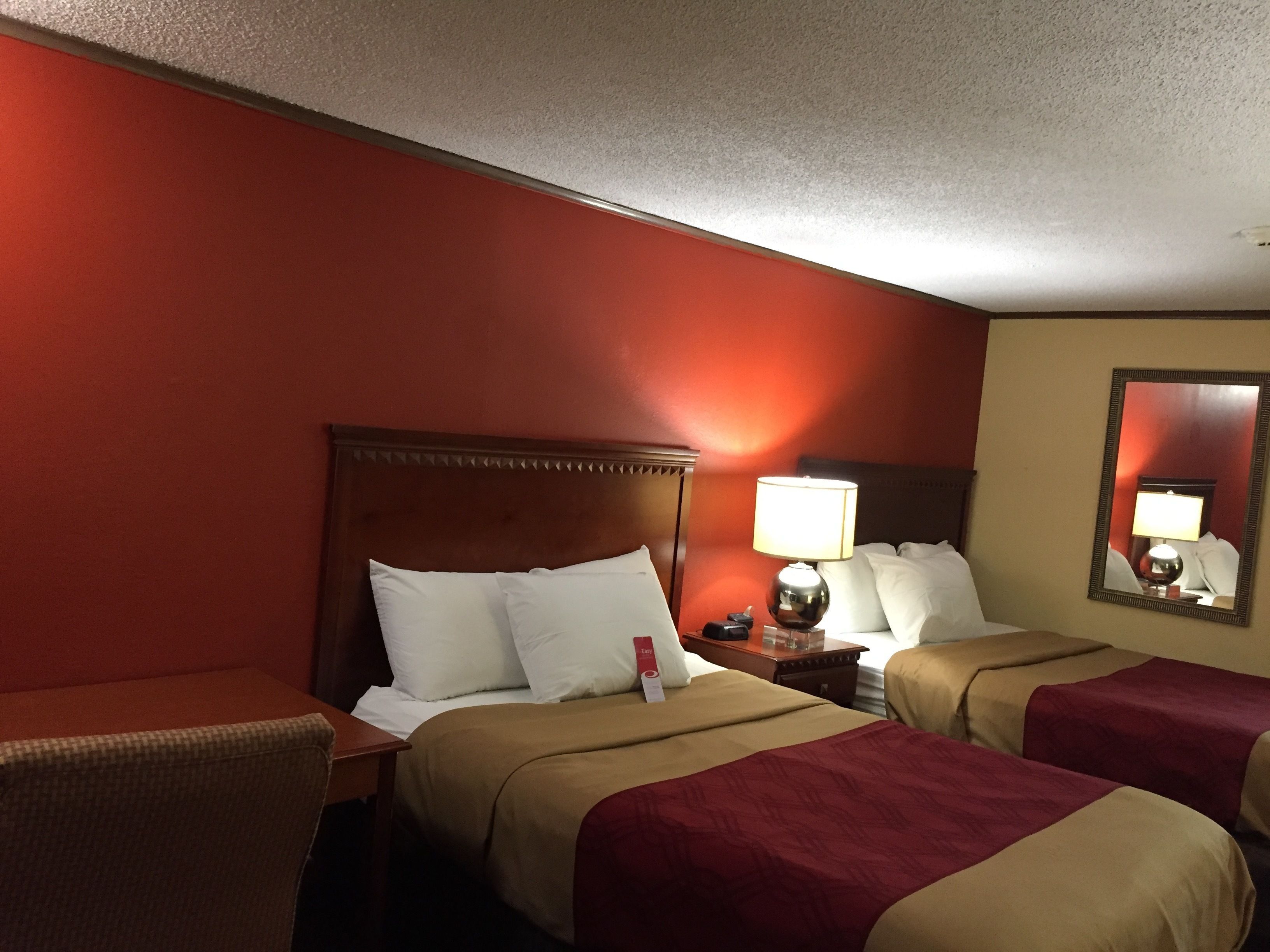 A hotel room with two beds, a nightstand, a lamp, and a mirror.