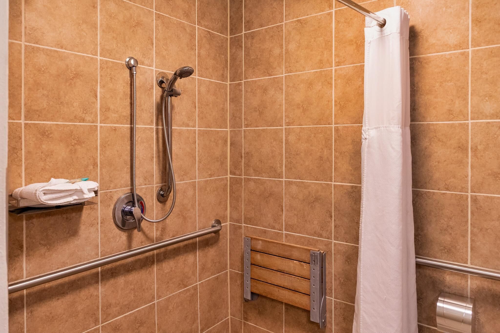 Un espacio de ducha con cabezal de ducha de mano, un perchero y una cortina de ducha.
