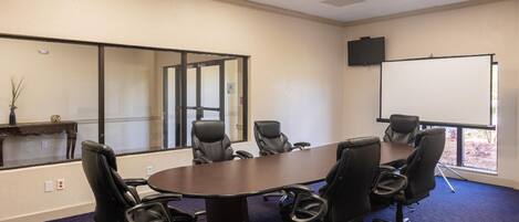 A conference room with a large table, six black chairs, a whiteboard, and a television on the wall.