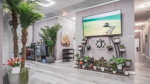 A modern lobby with a large TV screen, potted plants, and a wooden reception desk. - Cottonwood Suites Savannah Hotel & Conference Center (Pooler)