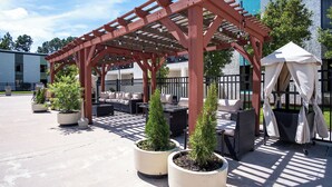 A covered outdoor seating area with a pergola, potted plants, and a white tent. - Cottonwood Suites Savannah Hotel & Conference Center (Pooler)