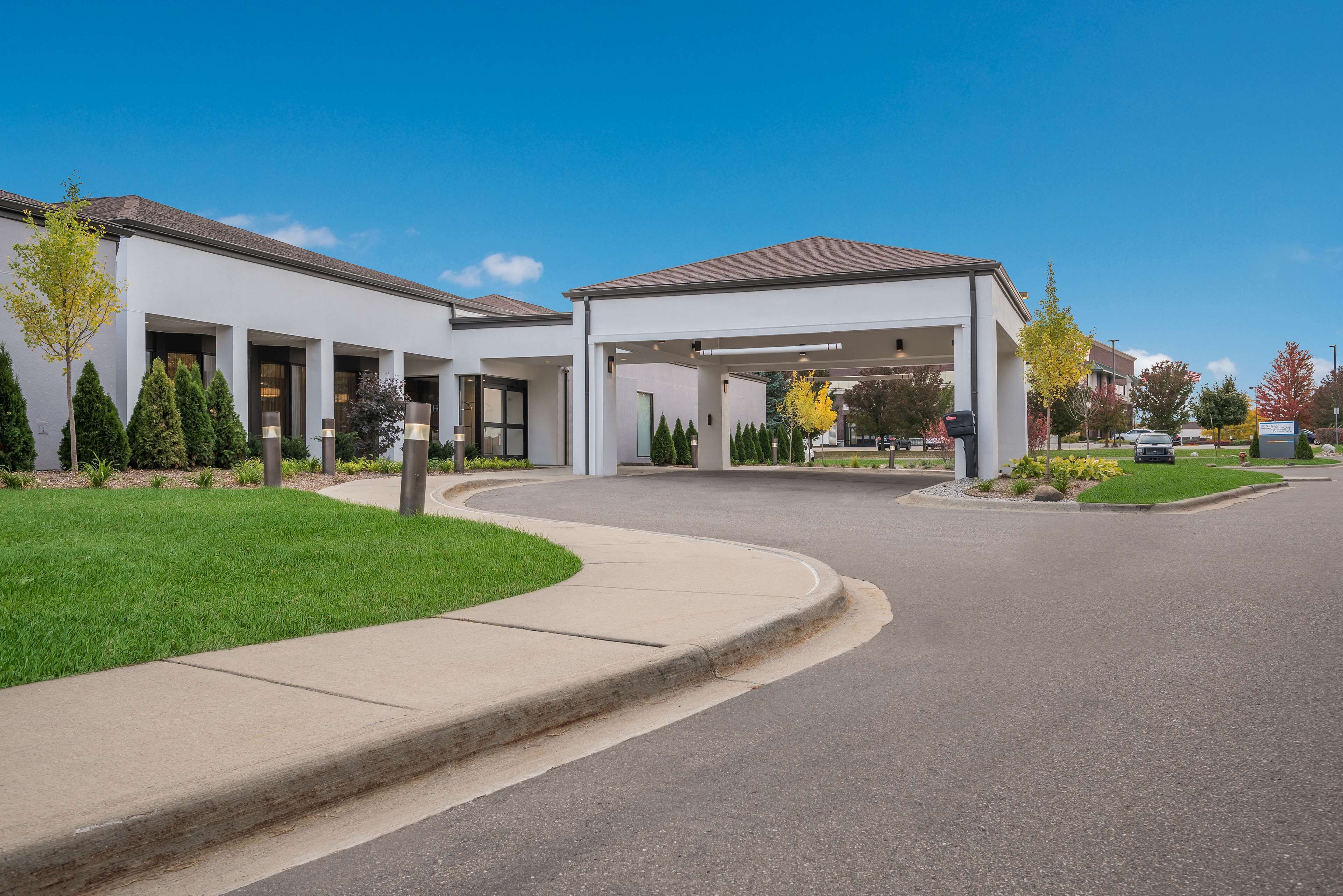A modern building with a covered parking area, a landscaped lawn, and a clear sky.