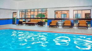 An indoor swimming pool with lounge chairs and tables, large windows, and a view of the outside building. - Sonesta Select Detroit Auburn Hills (Auburn Hills)