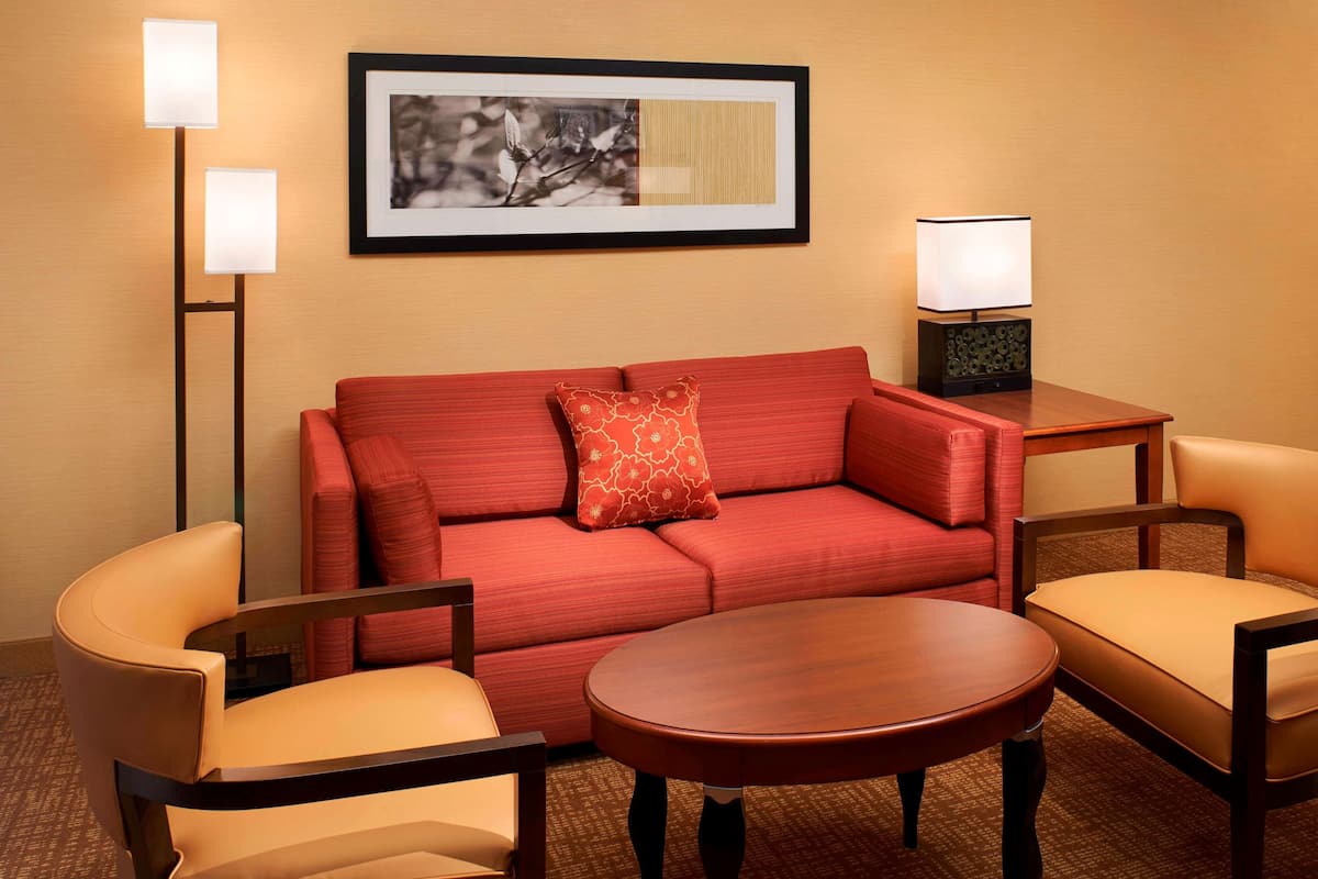 Ein Hotelzimmer mit einem roten Sofa, zwei Sesseln, einem Holztisch und einem gerahmten Bild an der Wand.