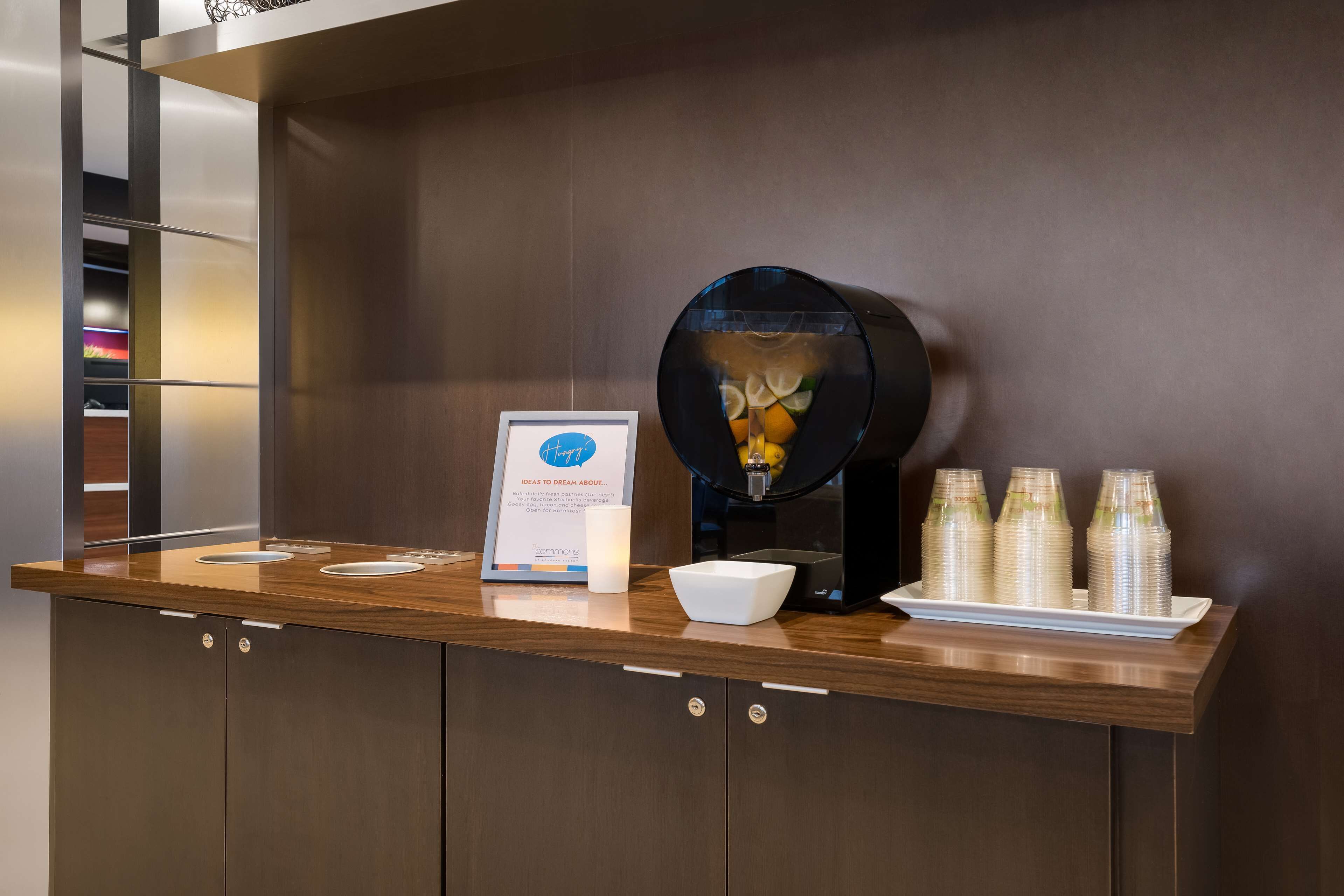 A reception area with a coffee machine, a framed sign, and stacked cups on a wooden counter.