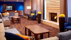 A hotel lobby with a sofa, armchairs, a fireplace, and a television screen. - Sonesta Select Detroit Auburn Hills (Auburn Hills)