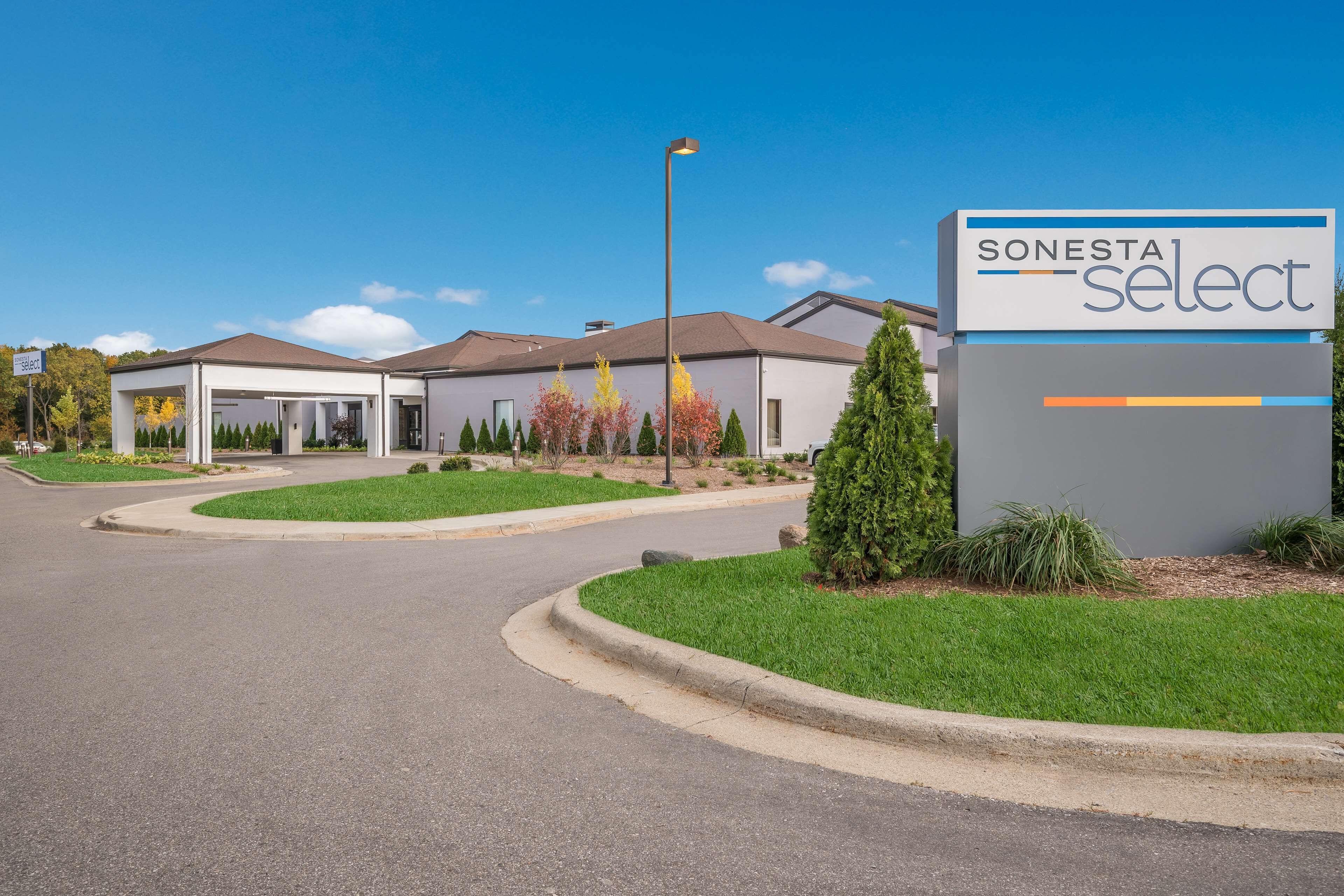 A Sonesta Select hotel with a modern design, featuring a well-maintained lawn, a clear sky, and a parking area.
