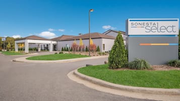 A Sonesta Select hotel with a modern design, featuring a well-maintained lawn, a clear sky, and a parking area.