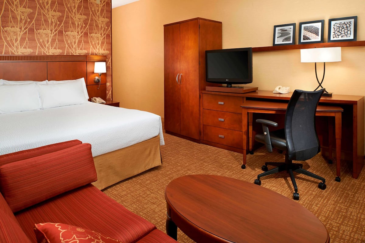 Ein Hotelzimmer mit einem Bett, einem Schreibtisch mit Computer, einem Stuhl, einem Kleiderschrank und einem Fernseher.