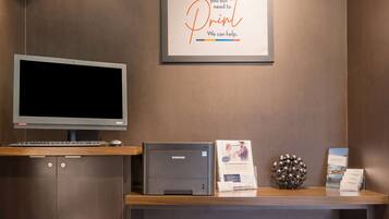 A Samsung printer on a desk with a framed sign above it, a monitor, and a decorative sphere.