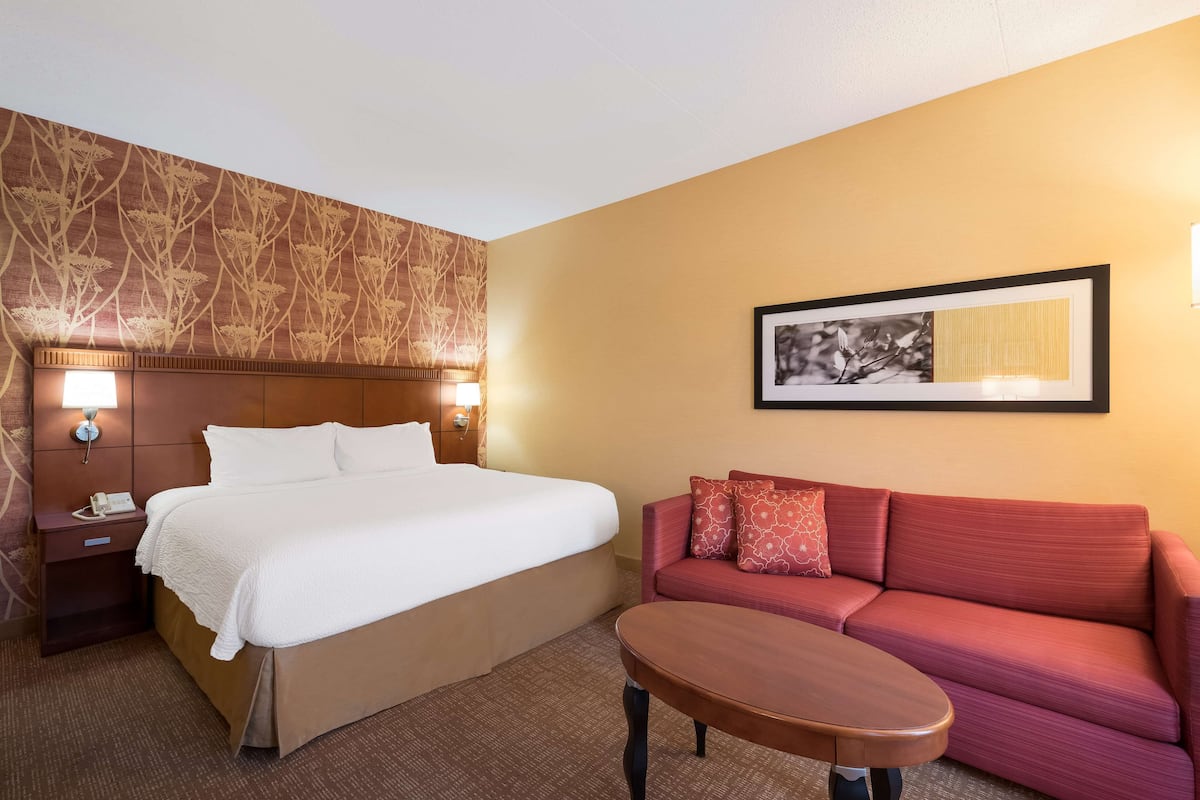 Ein Hotelzimmer mit einem Bett, einem roten Sofa, einem kleinen Tisch und einem gerahmten Bild an der Wand.