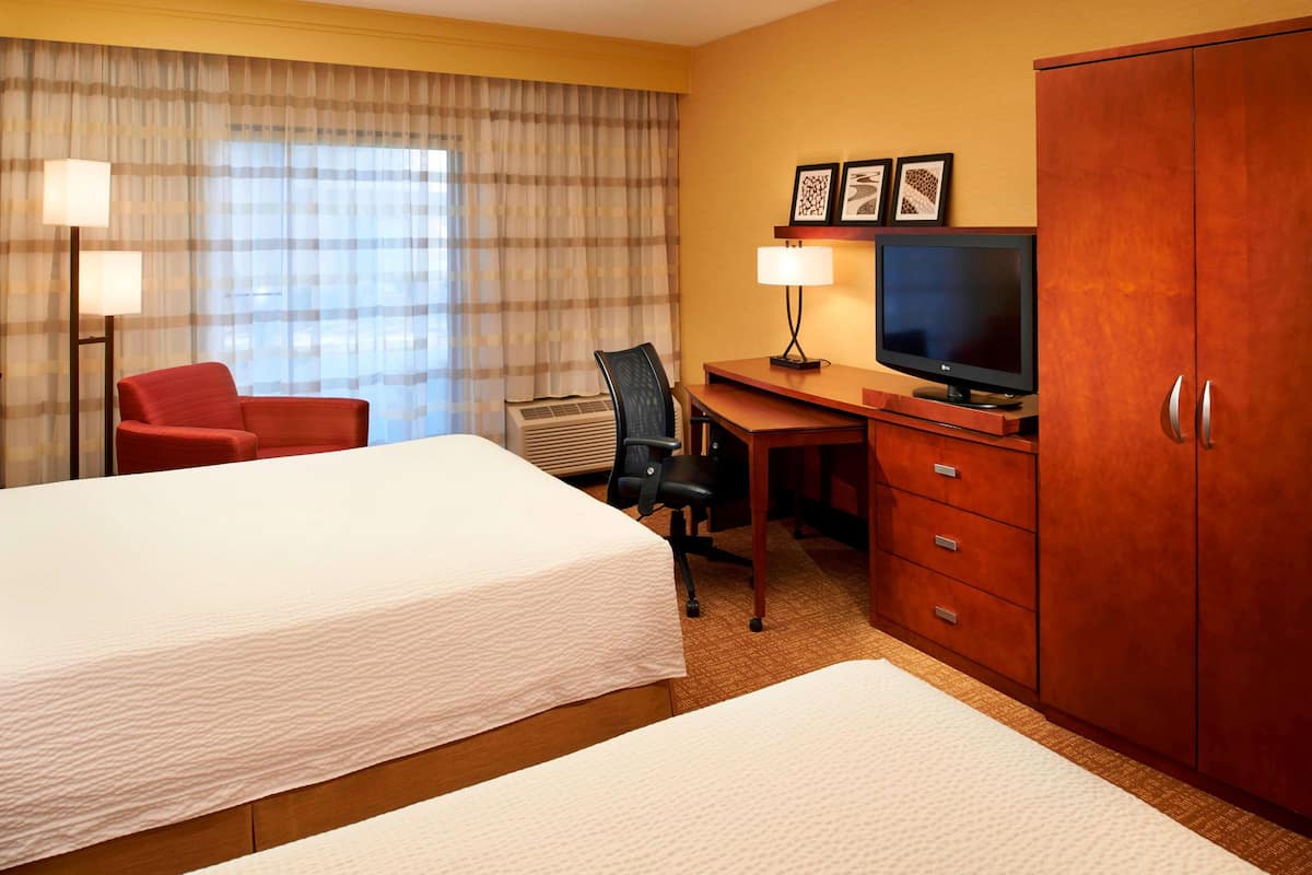 Ein Hotelzimmer mit zwei Betten, einem Schreibtisch mit Fernseher, einem Sessel und einem Kleiderschrank.