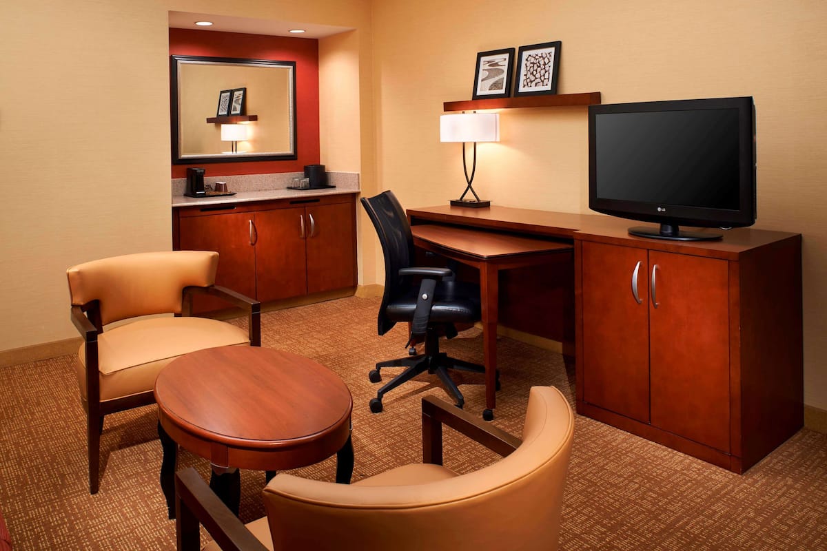 Ein Hotelzimmer mit Schreibtisch, zwei Stühlen, Fernseher, Lampe und Spiegel.