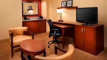 A hotel room with a desk, two chairs, a television, a lamp, and a mirror.
