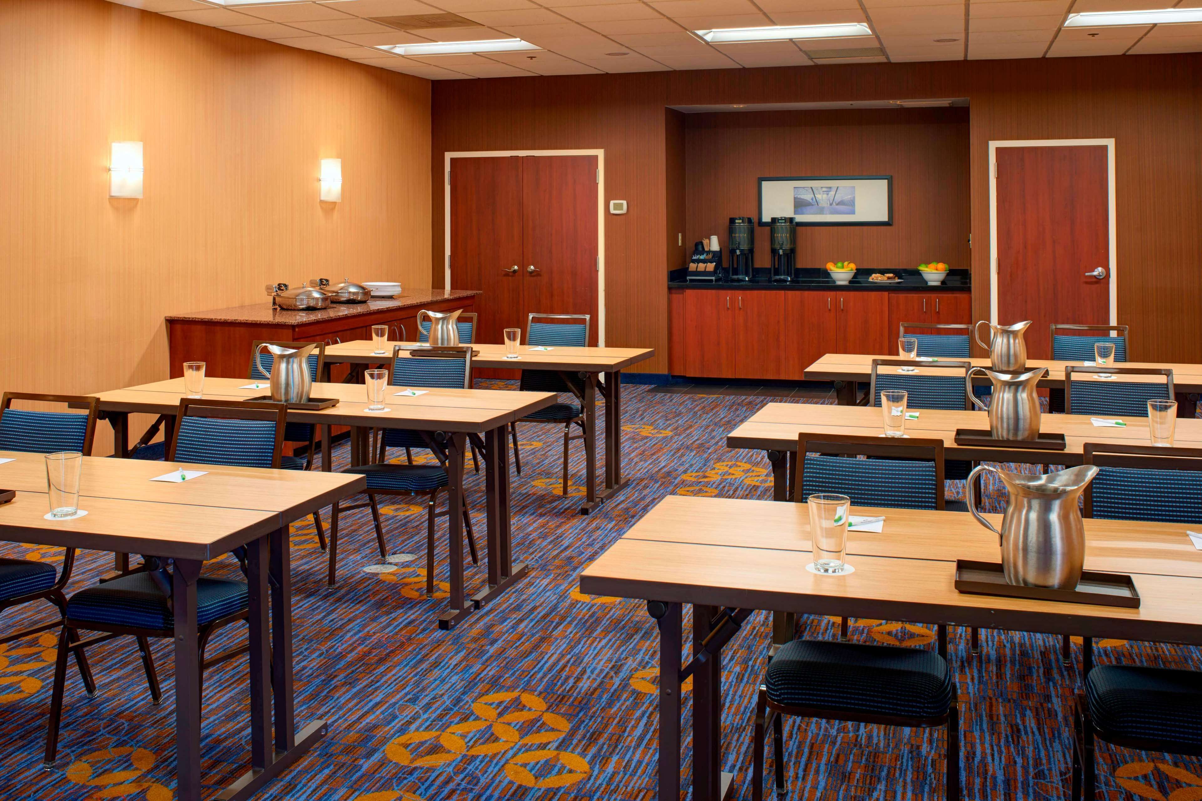 A conference room with multiple tables and chairs, a coffee station, and a television screen on the wall.