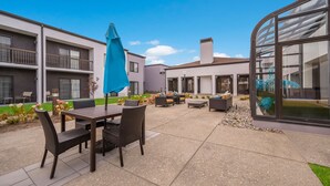 An outdoor patio area with a table and chairs, a blue umbrella, and a poolside lounge. - Sonesta Select Detroit Auburn Hills (Auburn Hills)