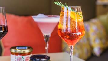 Una mesa con un vaso de bebida roja decorada con una ramita de romero, un frasco de mermelada y una botella de vino.