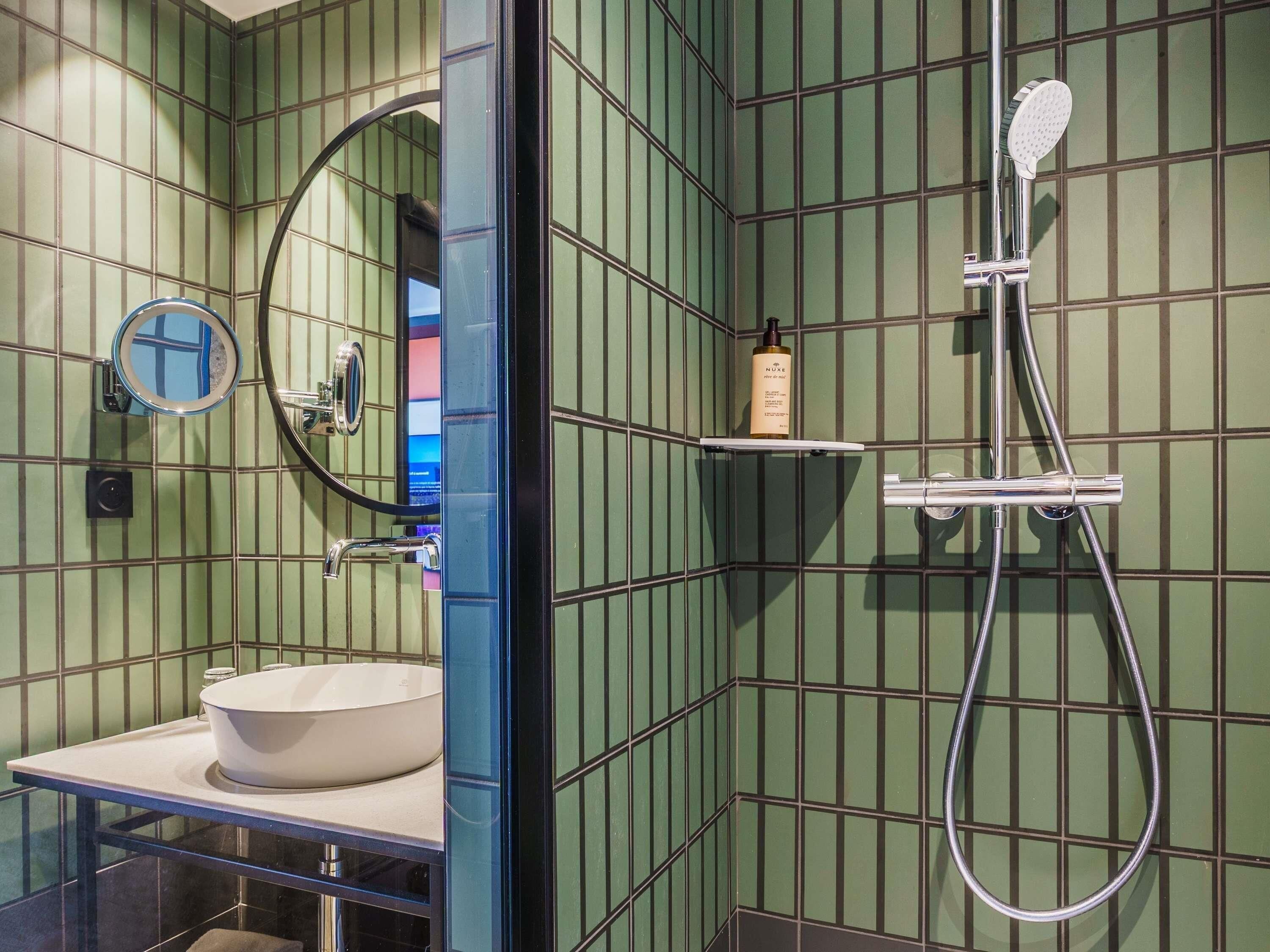 Une salle de bain avec un lavabo blanc, une douchette à main, un miroir et une étagère contenant des articles de toilette.