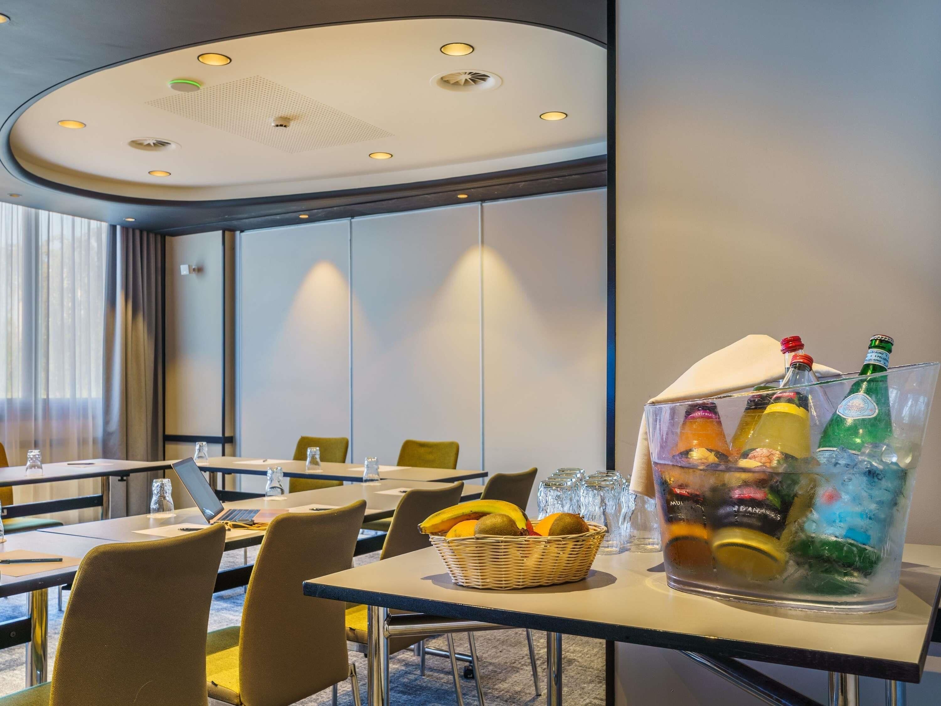 Ein Hotelkonferenzraum mit Tischen, Stühlen, einer Obstschale und einem großen Eimer mit Flaschen.