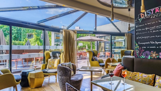 An outdoor cafe with modern furniture, large windows, and a menu board. - Mercure Dijon Centre Clemenceau (Dijon)