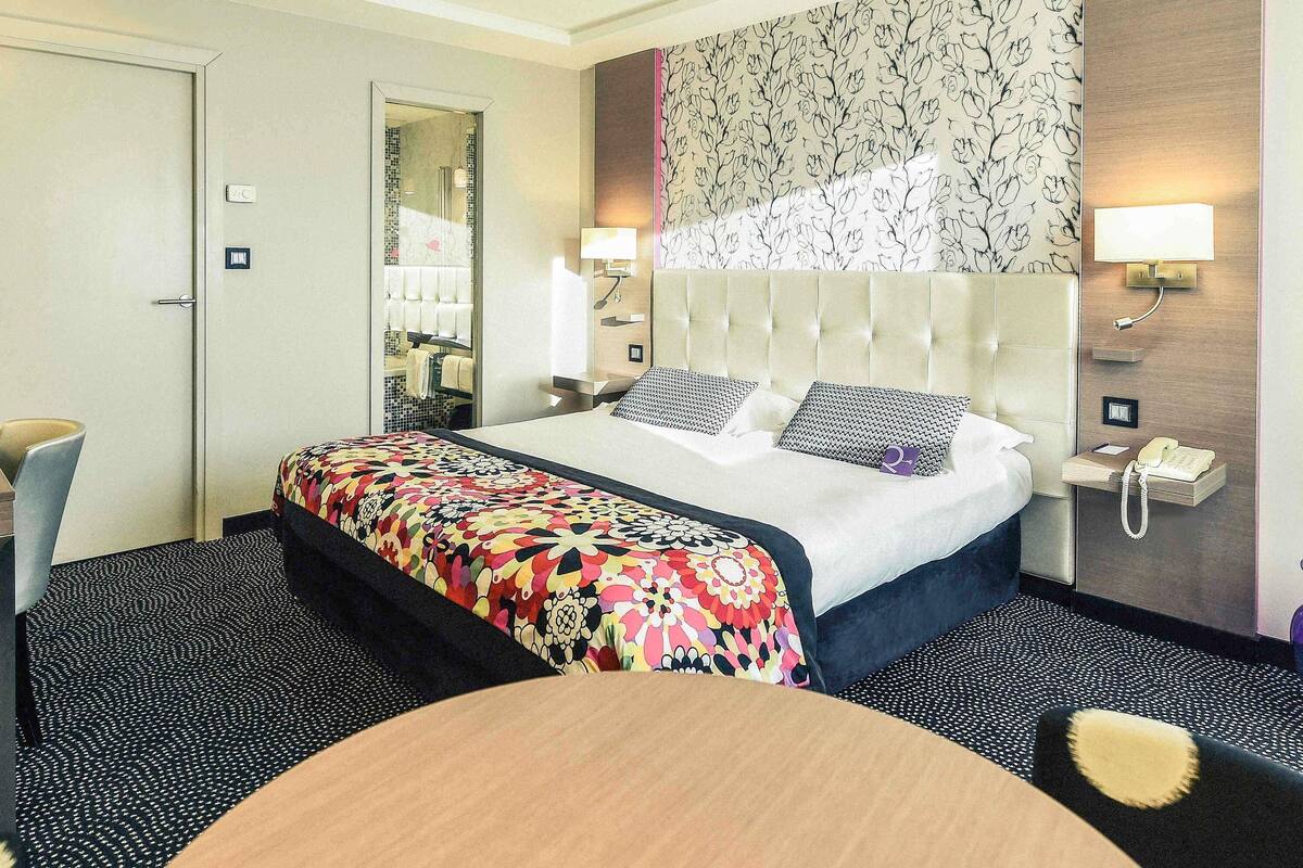 Una habitación de hotel con cama, mesita de noche, lámpara y espejo.