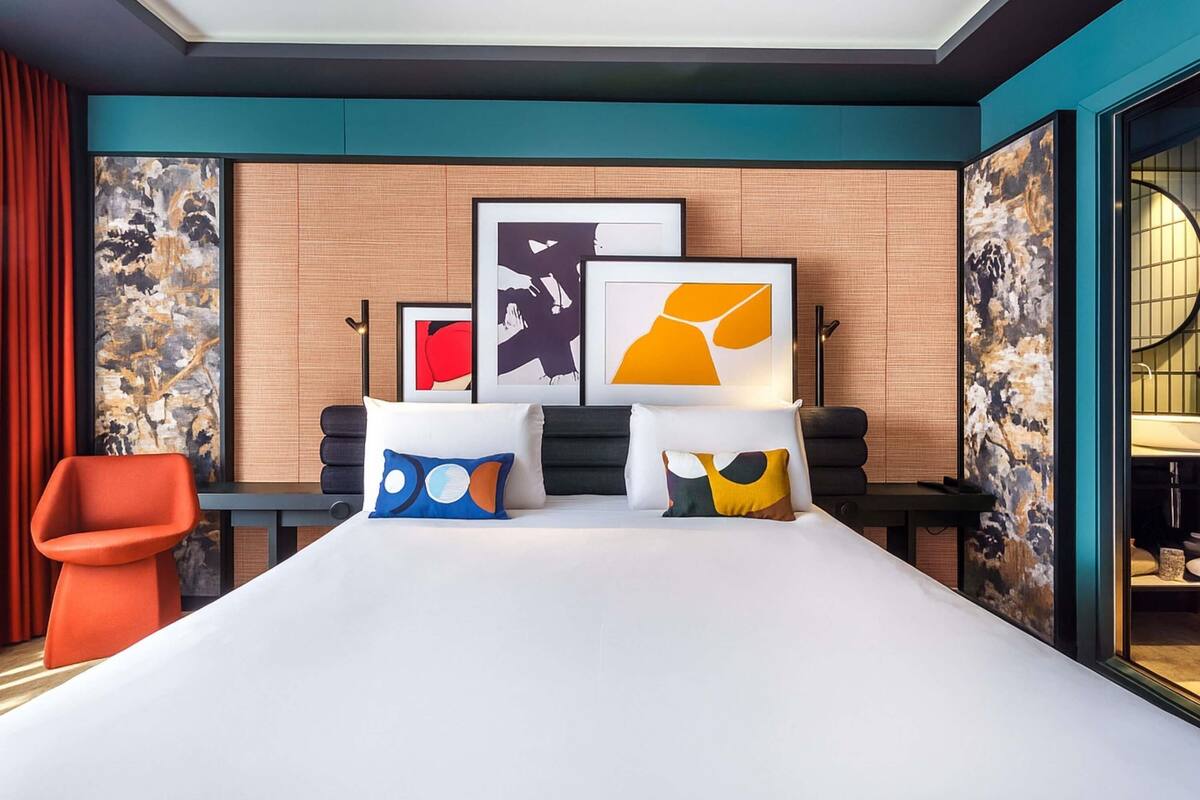 Una habitación de hotel moderna con una cama grande, obras de arte en las paredes y una silla roja.