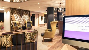 A modern interior with a central seating area, a large screen displaying 'WEB CORNE', and a wooden accent wall. - Mercure Dijon Centre Clemenceau (Dijon)