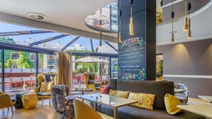 A modern restaurant with a glass ceiling, wooden flooring, and a variety of seating options including a sofa and chairs. - Mercure Dijon Centre Clemenceau (Dijon)