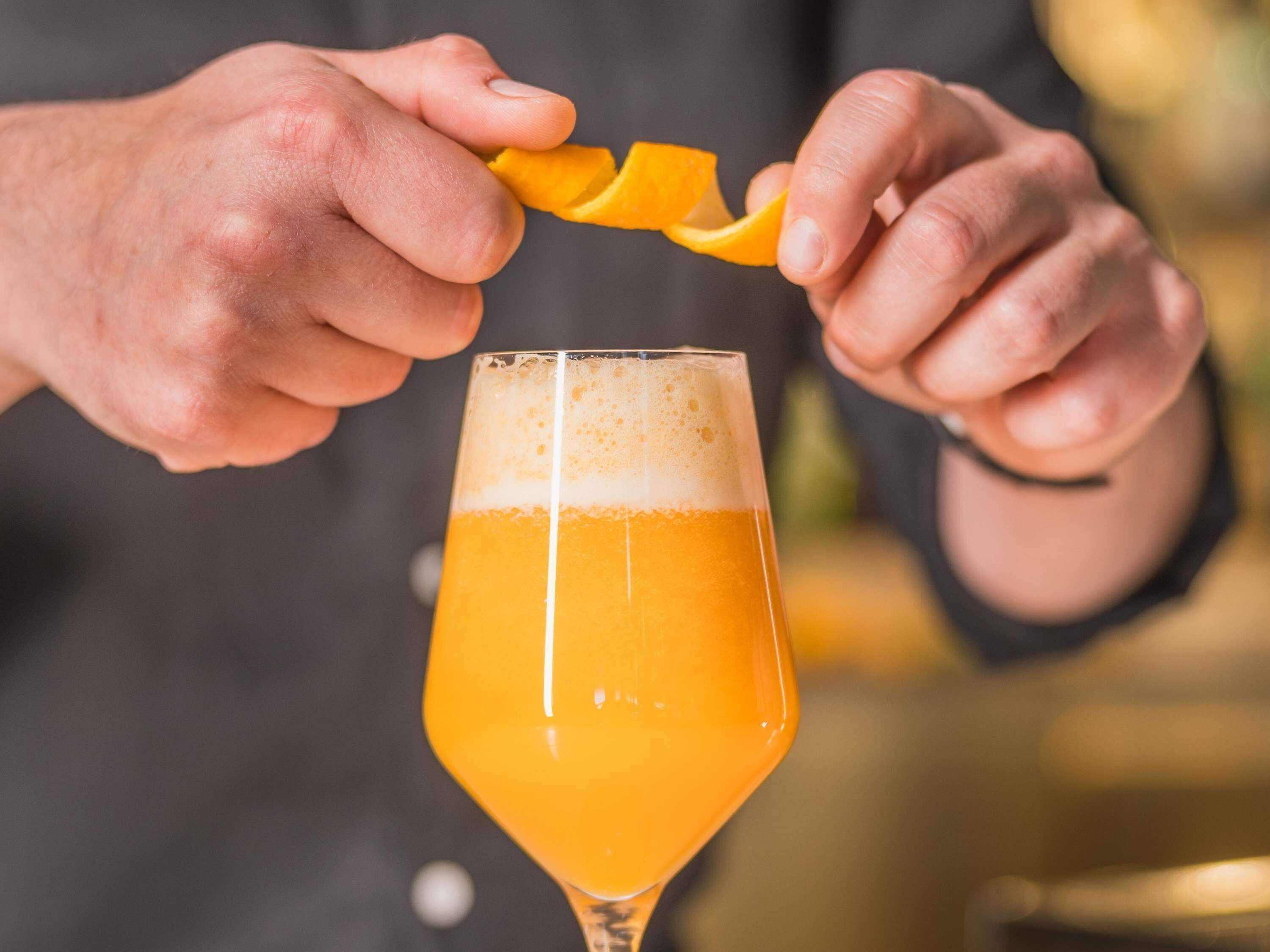 Une personne qui presse le zeste d’une orange dans un verre de bière.