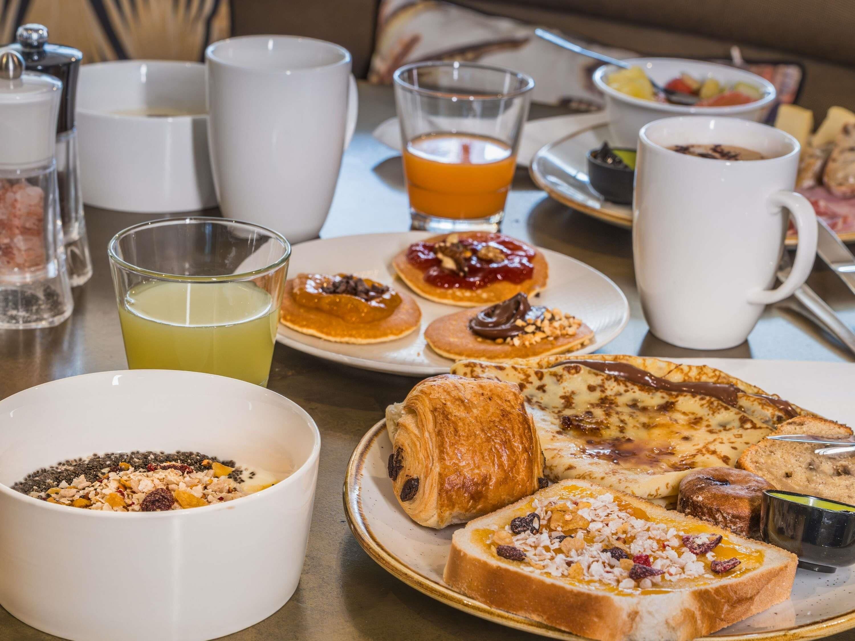 Un desayuno con varios pasteles, un tazón de cereal y un vaso de jugo de naranja.