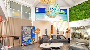 Een moderne hotellobby met een receptiebalie, een zithoek en een groot raam met uitzicht op zee.