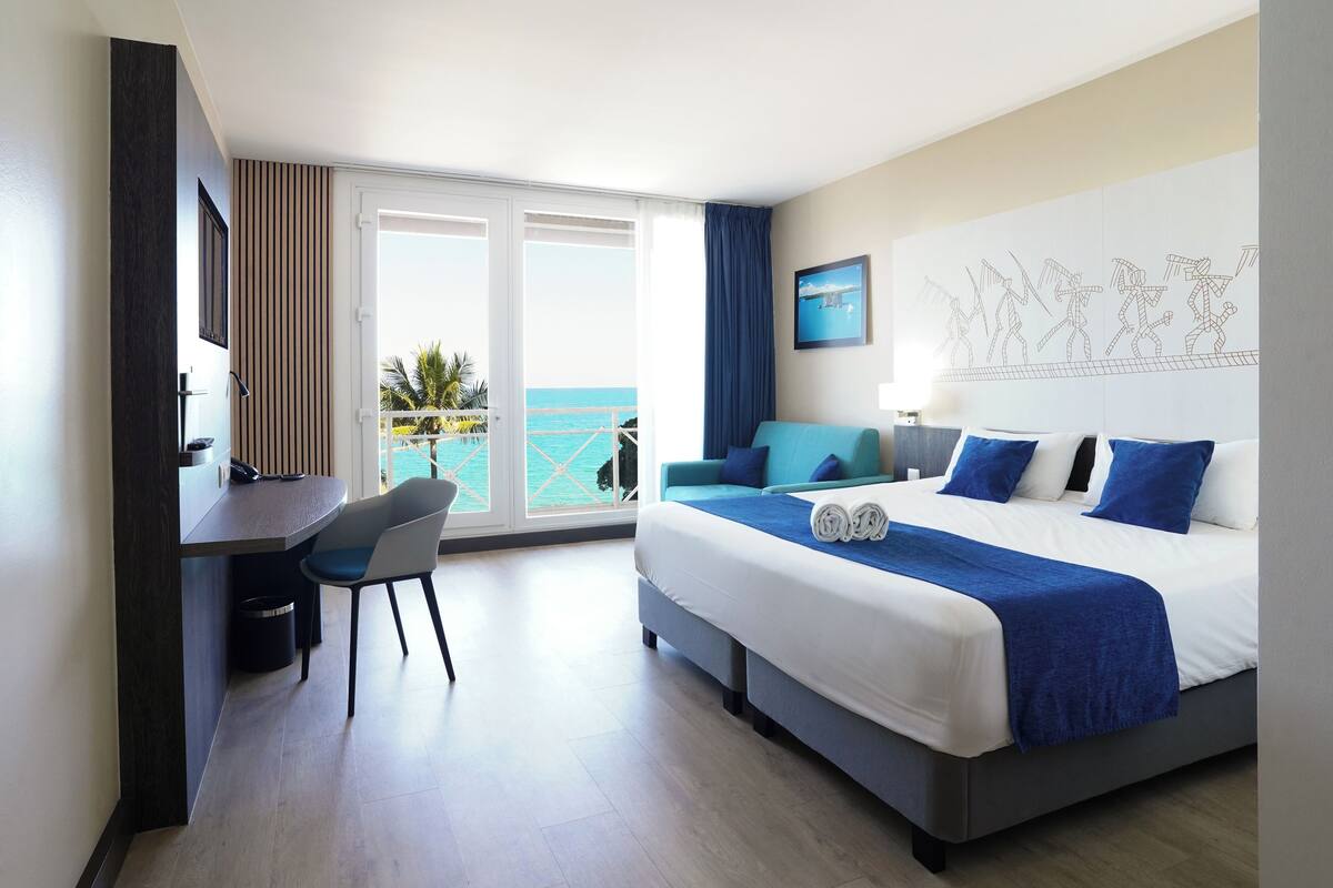 A hotel room with a bed, a desk, and a view of the ocean.