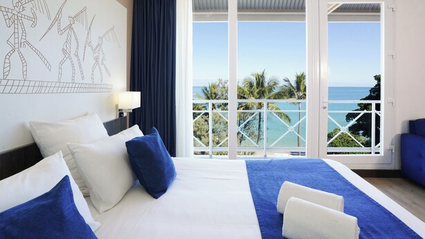 Een hotelkamer met een groot bed, uitzicht op de oceaan en een balkon met een hekwerk.