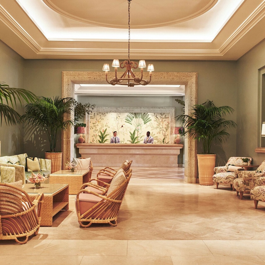A spacious lobby with a reception desk, wicker furniture, and potted plants.