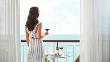 A woman standing by a balcony with a table set for a meal, overlooking a body of water.
