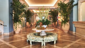 A spacious lobby with a central round table surrounded by ornate chairs, flanked by large potted plants and a grand staircase. - Four Seasons Resort Palm Beach (Palm Beach)