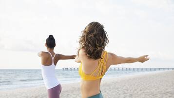 Two individuals exercising on a beach with a pier in the background.