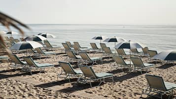 Na praia, areia branca, espreguiçadeiras, guarda-sóis