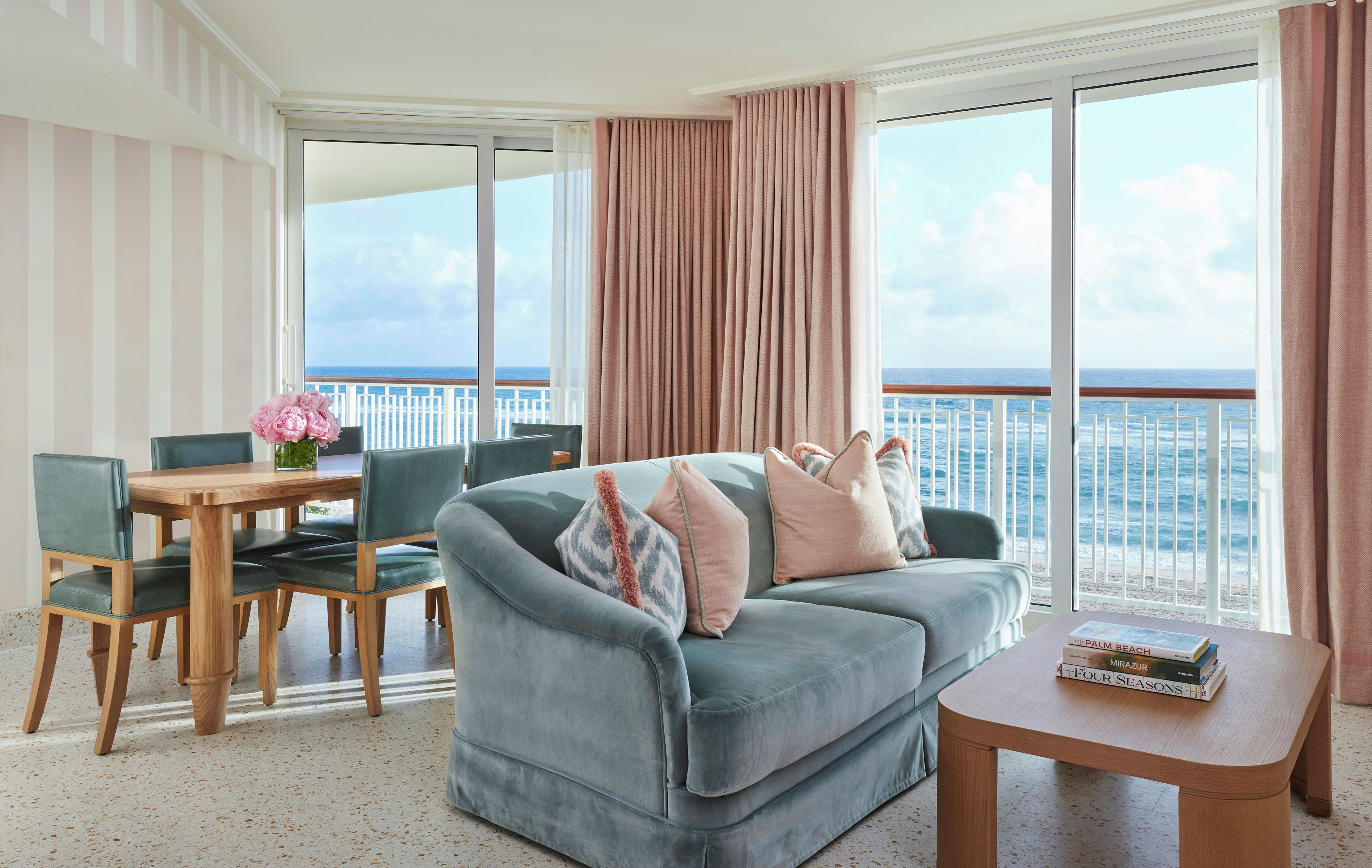 A balcony with a view of the sea, a sofa, a table with books, and a chair.
