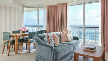 A balcony with a view of the sea, a sofa, a table with books, and a chair.