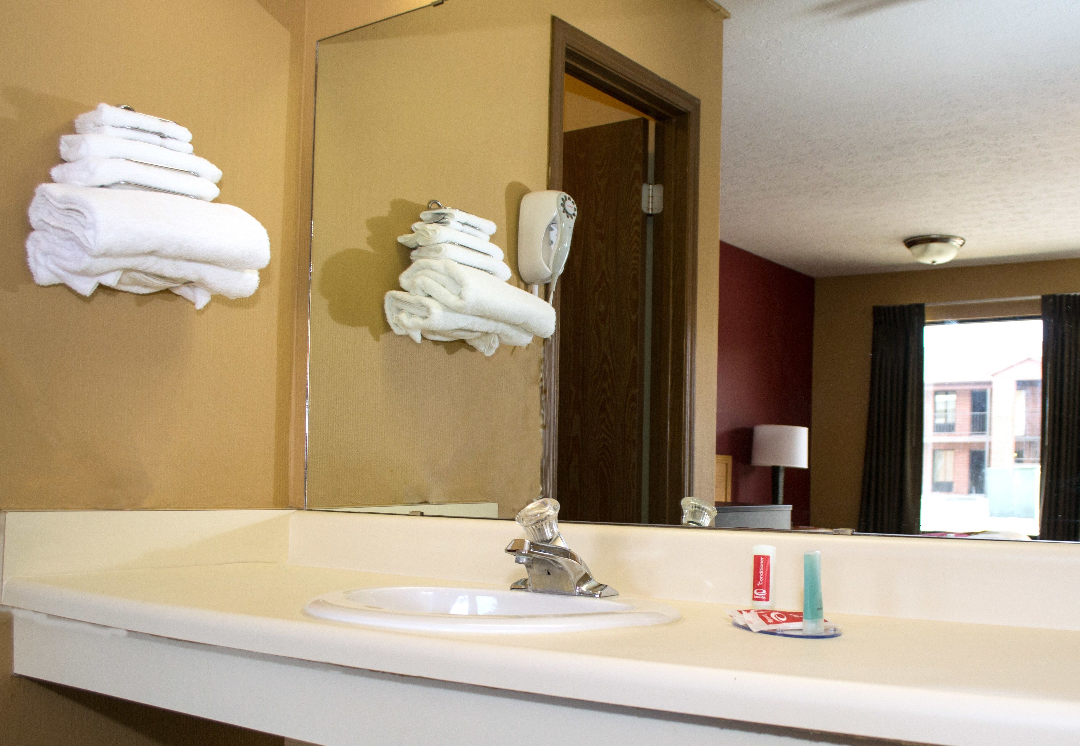 A hotel bathroom with a sink, mirror, and stacked towels.