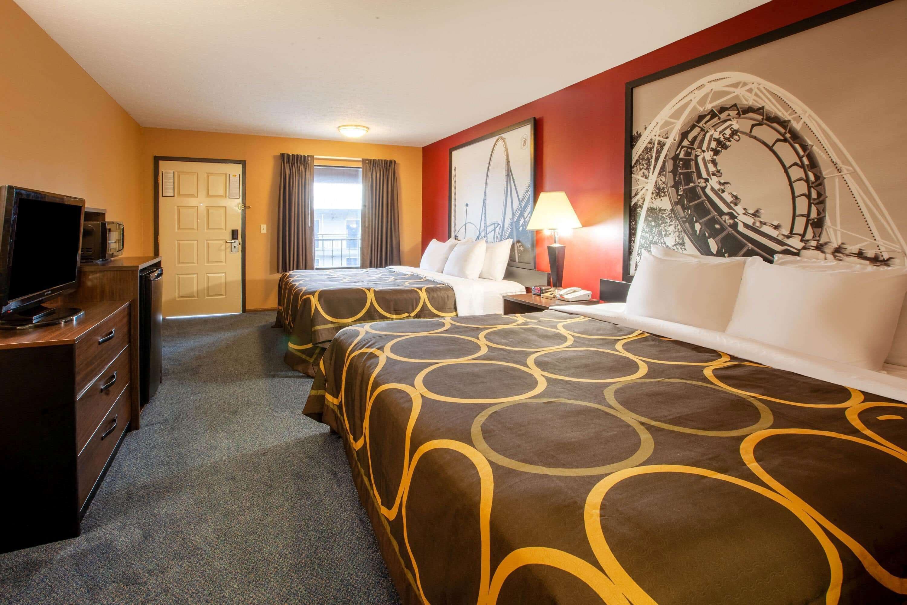 A hotel room with two beds, a desk with a television, a lamp, and a large framed picture on the wall.