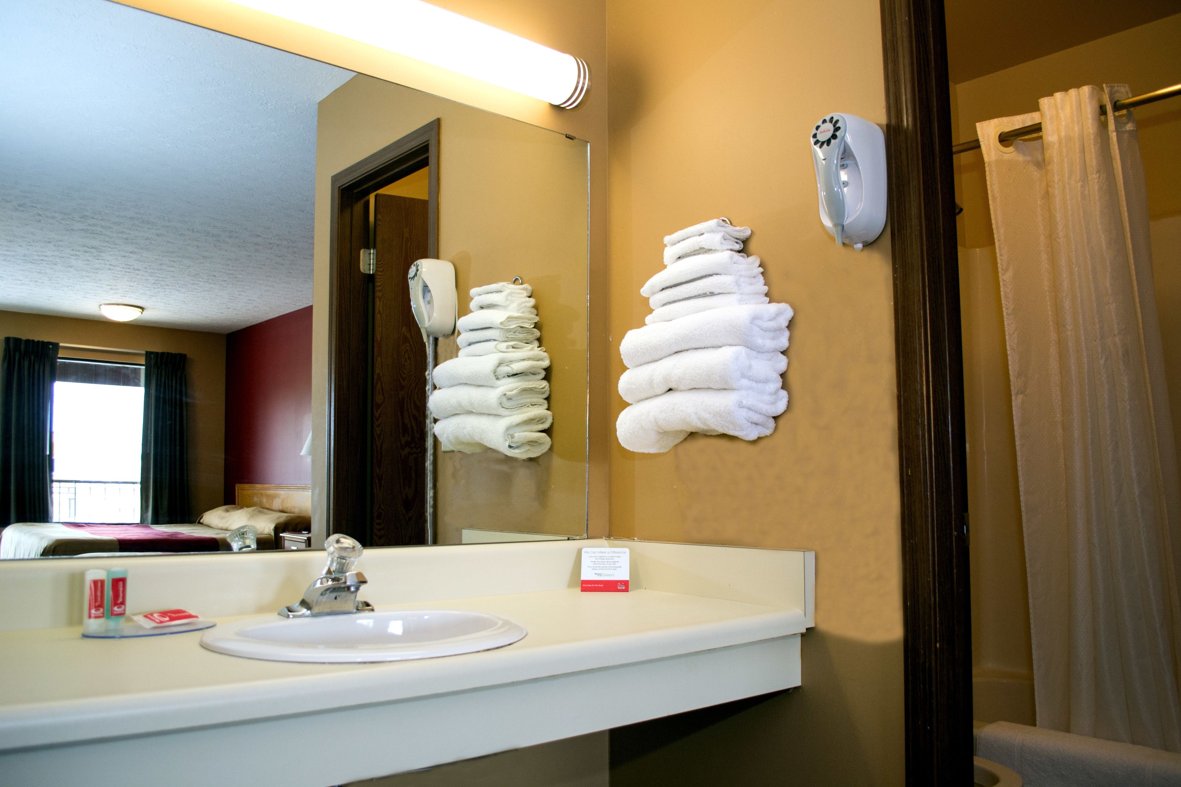 Un baño de hotel con lavabo, espejo, dispensador de toallas y cortina de ducha.