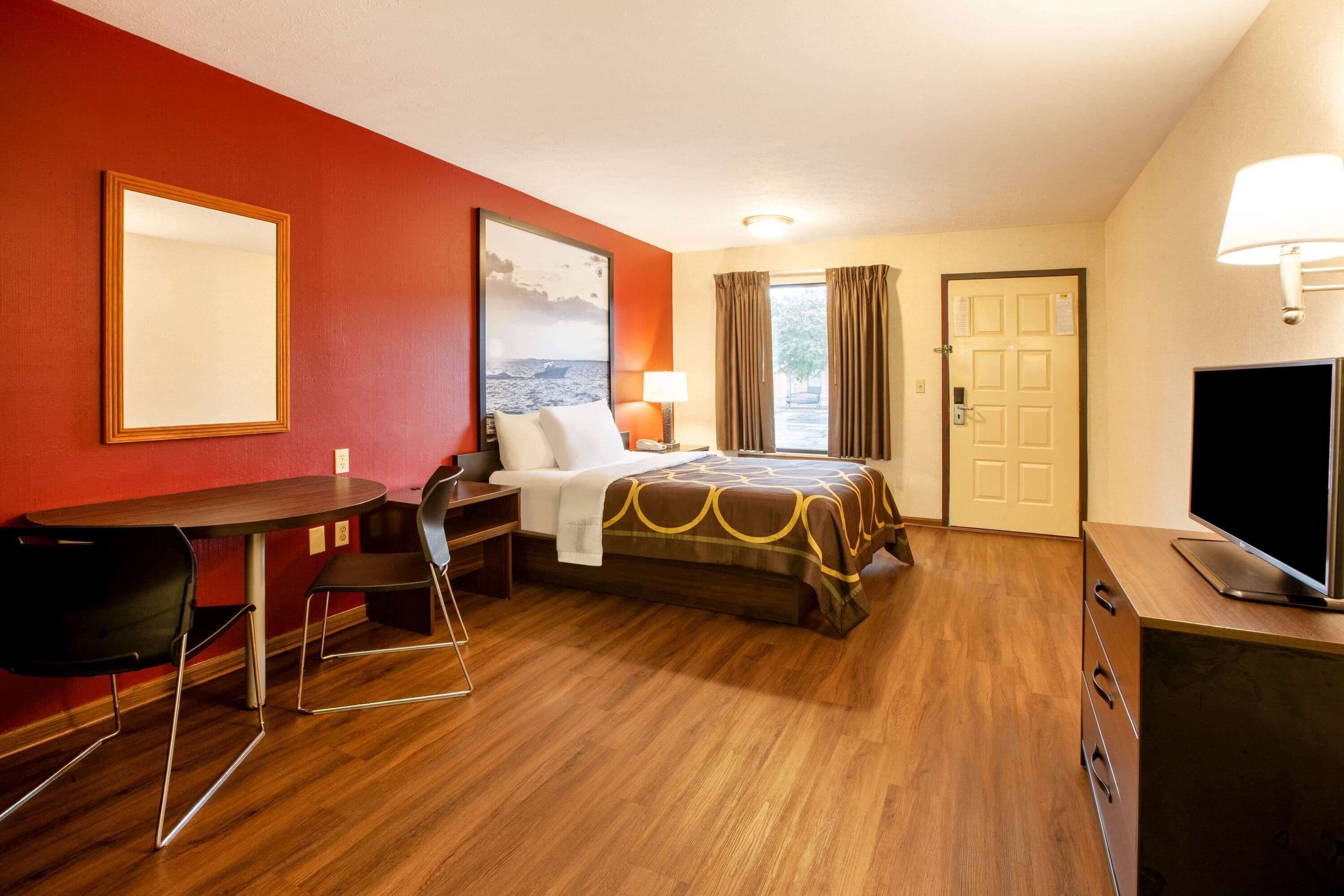 Habitación de hotel con cama, escritorio, silla, televisor y ventana con cortinas.