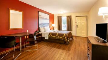 Habitación de hotel con cama, escritorio, silla, televisor y ventana con cortinas.
