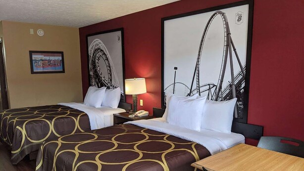 A hotel room with two beds, a wooden table, and a wall with a roller coaster picture. - Super 8 by Wyndham Sandusky (Sandusky)