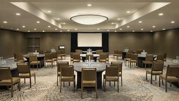 A conference room with round tables and chairs, a large screen, and a carpeted floor.