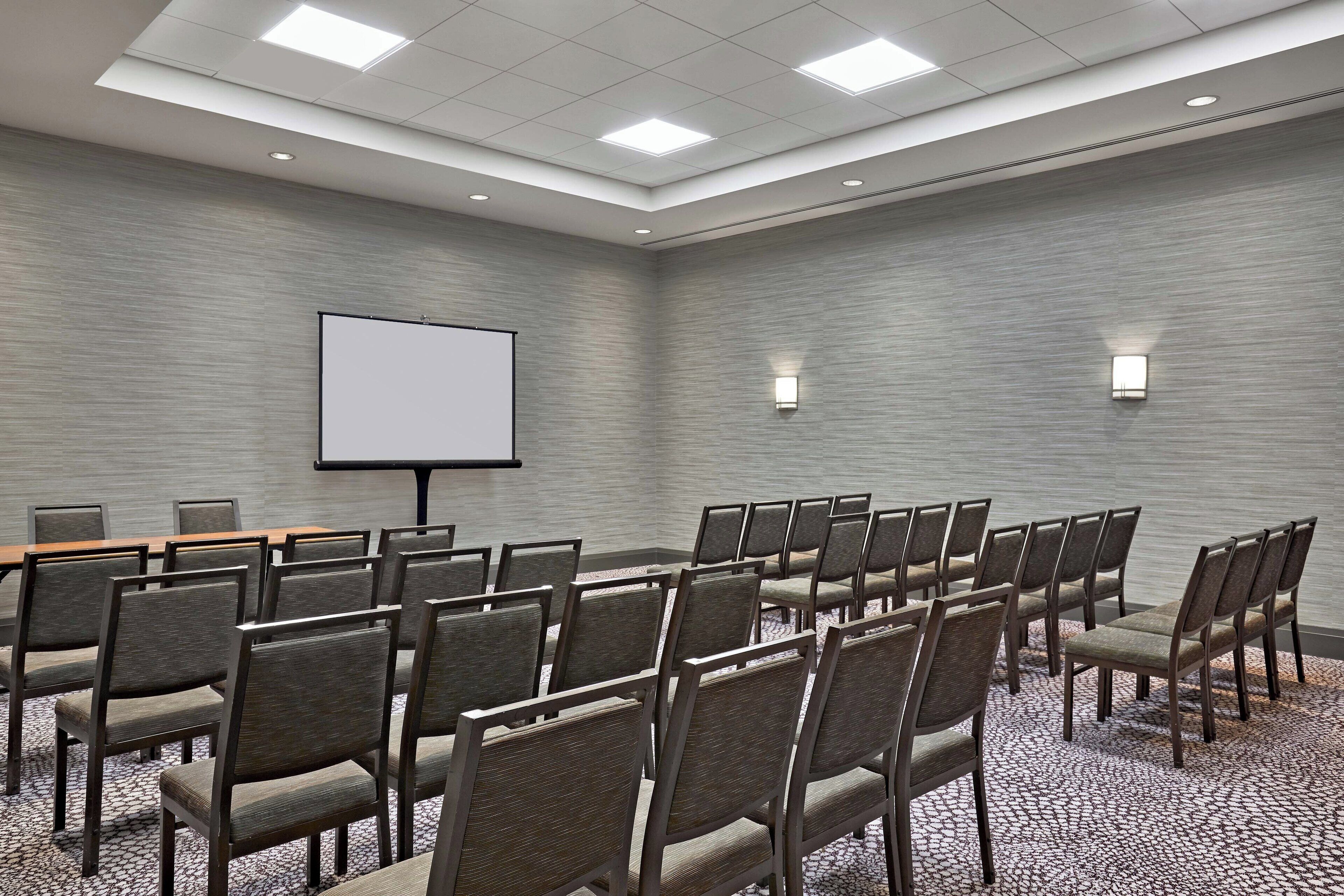 A conference room with rows of chairs, a projector screen, and a carpeted floor.