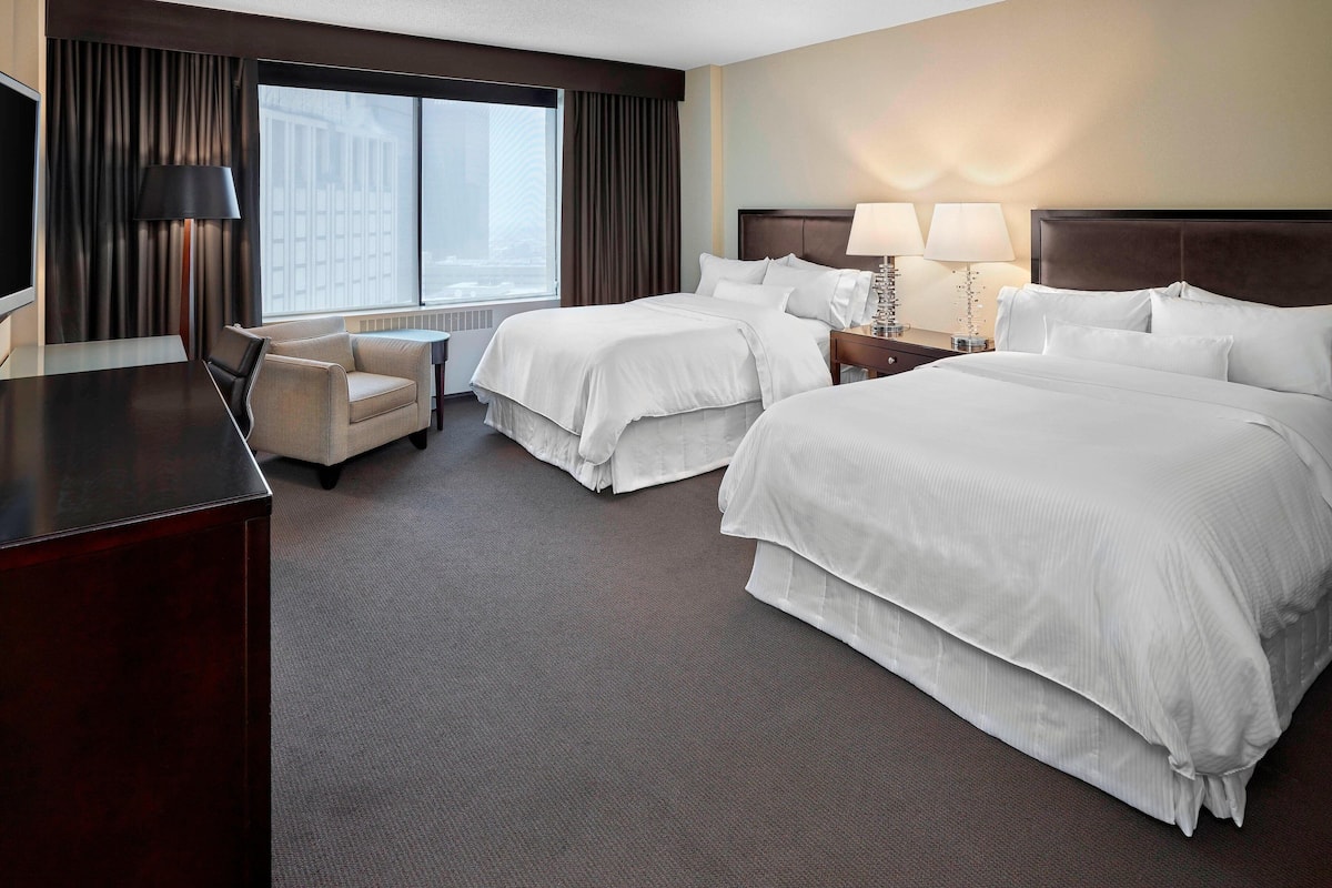 A hotel room with two beds, a desk, a chair, and a large window with curtains.